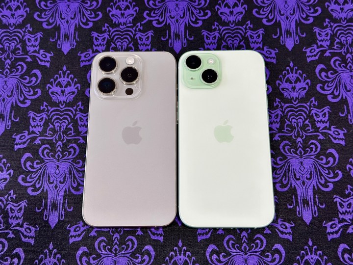 Ein iPhone 15 Pro aus natürlichem Titan (links) und ein grünes iPhone 15 auf einem Haunted Mansion-Tapeten-Tischset.