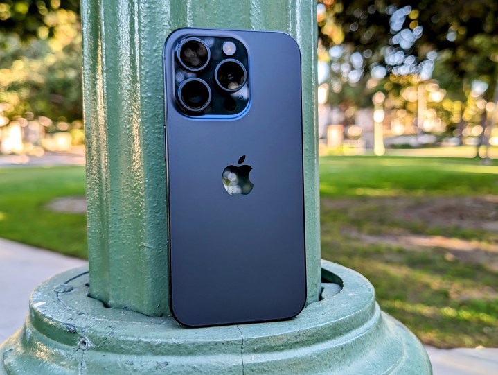 Blaues Titan-iPhone 15 Pro lehnt an einem Laternenpfahl im Park.