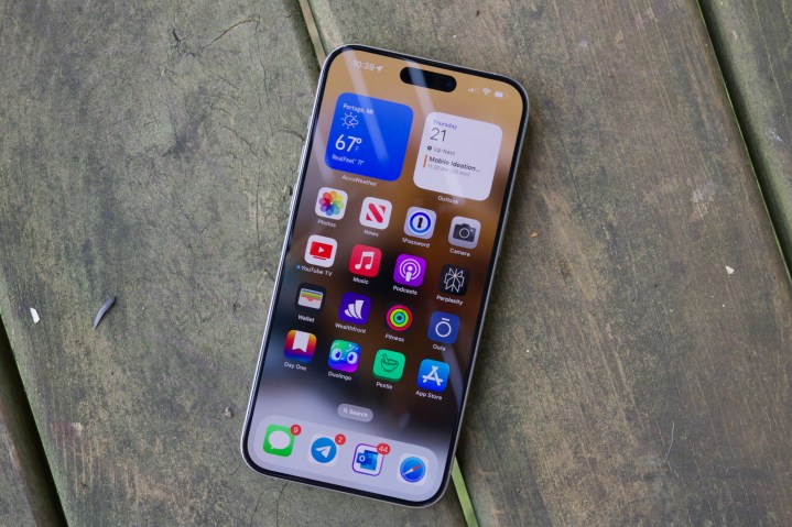 Ein iPhone 15 Pro Max, das mit eingeschaltetem Display auf einem Holzboden liegt.
