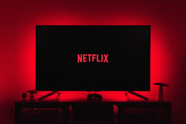 Das Netflix-Logo wird auf einem Fernsehbildschirm angezeigt, während rote Lichter die Wand dahinter beleuchten.