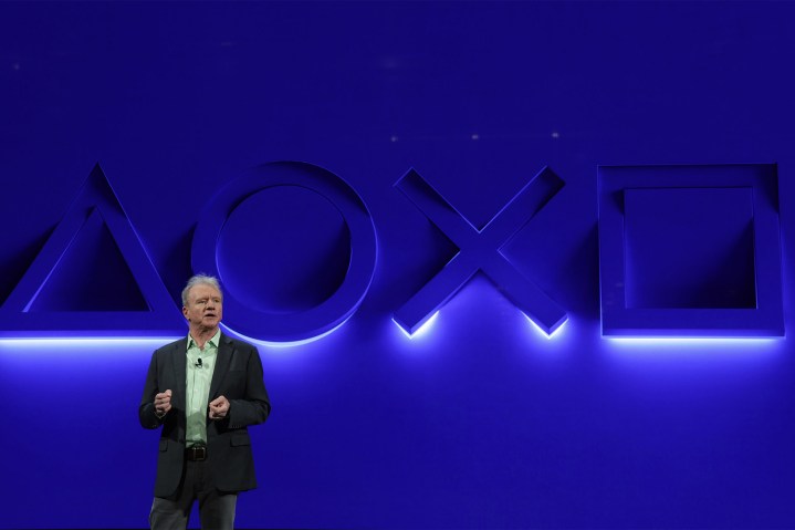Jim Ryan, CEO und Präsident von Playstation, steht vor einer blauen Wand mit beleuchteten Playstation-Tastensymbolen.