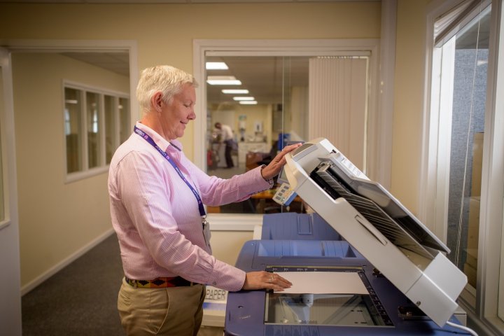 Eine Person hält den Deckel und legt ein Dokument in einen großen Bürokopierer.