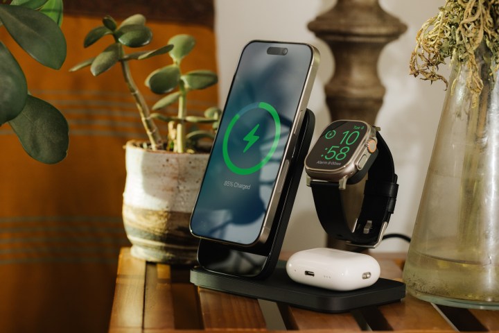 Schwarzer Nomad Stand One Max-Ladeständer auf einem Haushaltstisch mit angedocktem und aufgeladenem iPhone, Apple Watch Ultra und AirPods Pro.