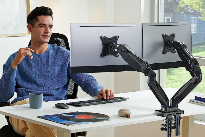 Mann benutzt zwei Monitorarme auf seinem Schreibtisch.