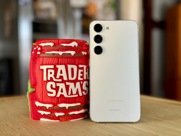 Samsung Galaxy S23 in Creme neben einem Weihnachts-Tiki-Becher von Trader Sam.