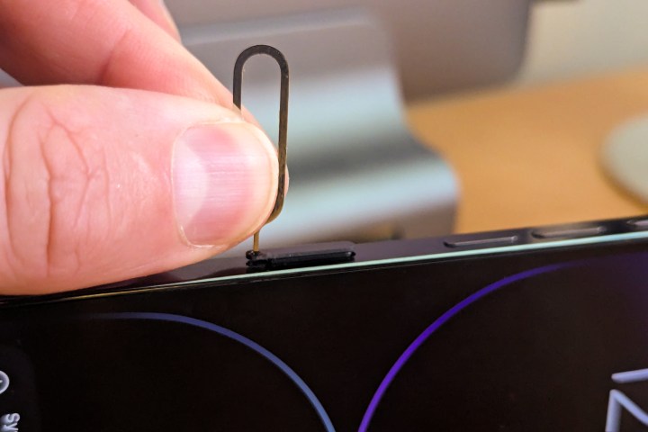 Mit Finger und Daumen wird das SIM-Auswurfwerkzeug in das SIM-Fach eines iPhone 14 Pro Max gedrückt.