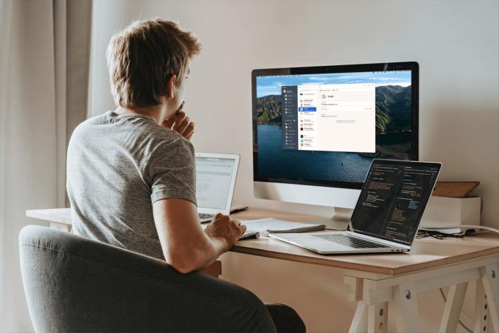 Eine Person verwendet 1Password auf einem Desktop-All-in-One-Computer, während sie an einem Schreibtisch sitzt. Neben ihr auf dem Schreibtisch stehen zwei Laptops.