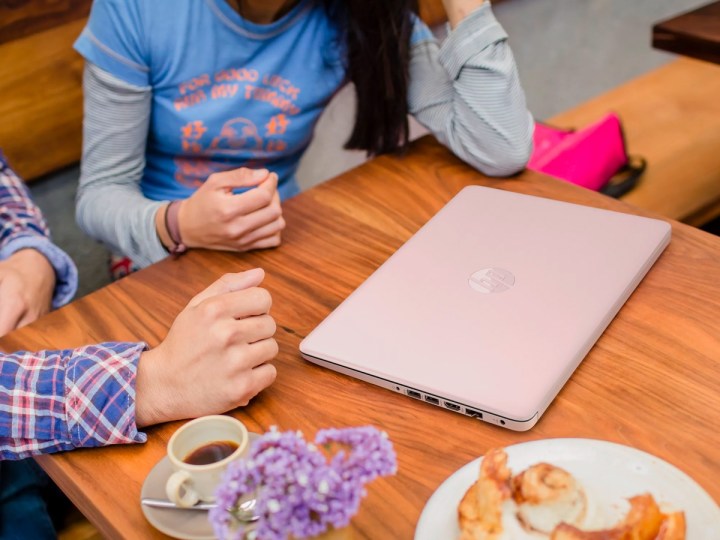 Ein rosa Modell des 14-Zoll-Laptops HP Stream steht auf einem Cafétisch, während sich Leute unterhalten.