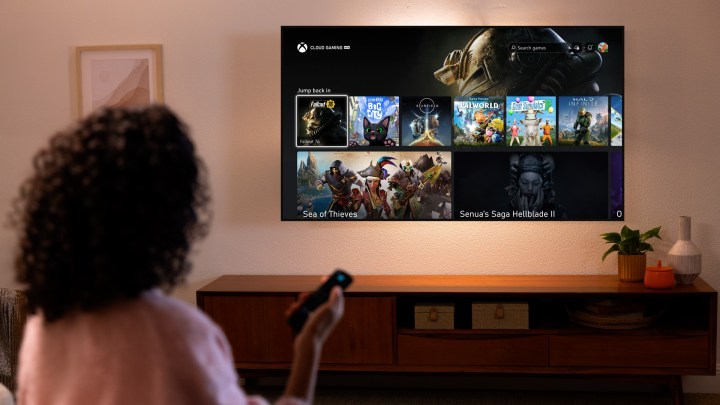 Eine Frau hält eine Fernbedienung in der Hand und schaut auf ein Amazon Fire TV mit der Xbox-App darauf. Es steht im Cloud Gaming-Menü mit Fallout 76, Senua's Saga: Hellblade 2 und mehr darauf.